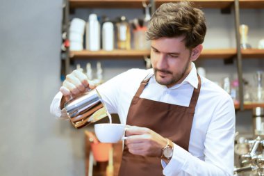 Yakışıklı beyaz garson küçük işletme sahibi barista kafede sütlü kahve ya da cappuccino yapan sütlü kahve yapıyor. Küçük işletme sahibi veya KOBİ kavramı ile çalışan adam.