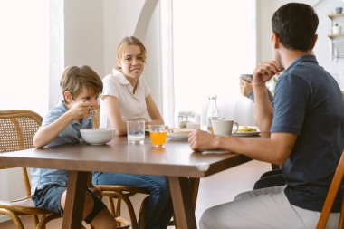 Ailesi olan küçük, mutlu beyaz bir çocuk evde birlikte kahvaltı yapıyor. Sevimli küçük çocuk yemeğin tadını çıkarıyor. Aile birlikte vakit geçirmekten zevk alıyor..