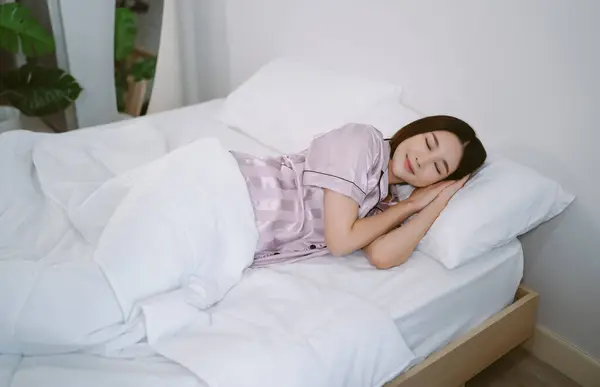 Top view of beautiful young Asian woman smiling wearing satin pajamas while sleeping in bed and relax in the morning. Lady enjoy sweet dreams, good rest at home and calm atmosphere. Lifestyle concept