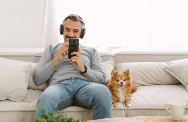 Orta yaşlı beyaz bir adamın portresi kanepeye oturmuş, kablosuz kulaklıklarla akıllı telefonlardan müzik dinliyor, arkasına yaslanıp güzel chihuahua köpeğiyle oturuyor. Arkadaş Canlısı Konsept