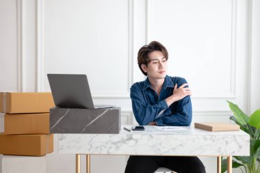 Asyalı serbest çalışan yakışıklı bir adam çalışma masasında oturuyor ve asgari ev ofisinde çalışırken gözlerini kaçırıyor. Etrade, çevrimiçi pazarlama paketleme. Başlangıçta küçük işletme sahibi kavramı