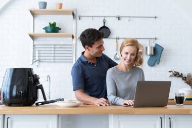 Romantik orta yaşlı çift mutfak odasında dizüstü bilgisayar kullanırken kucaklaşıyorlar. Mutluluk, romantik insanların sevgiyle sarılmaları, birlikte zaman geçirmeleri. Evdeki yeni normal iş hayatı.