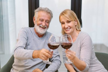 Mutlu yaşlı çift yemek masasında kırmızı şarap kadehleriyle kutlama ve tezahürat yapıyor. Romantik çift evde yemek yiyor. Birlikte vakit geçirmek..