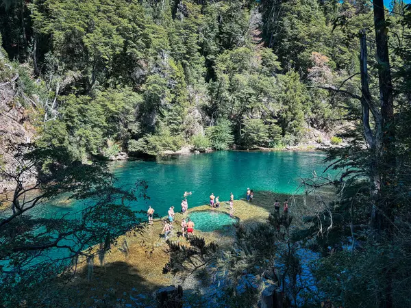 İnsanlar sık orman ve kayalık kıyılarla çevrili sakin bir zümrüt yeşili nehirde yüzüyor ve yürüyor. Uçurumlar ve parlak mavi bir gökyüzü verimli bir yaz manzarası yaratıyor.