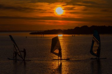 Gün batımında sakin bir gölde rüzgar sörfü, tatil sporu.