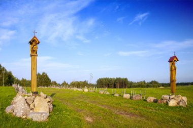 A village road through meadows to the church surrounded by stones, roadside chapels as a religious symbol
