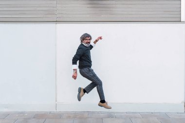 Mature man looking at camera while jumping on footpath
