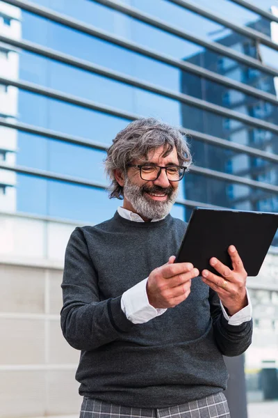 Happy mature handsome business man using a digital tablet outside office building