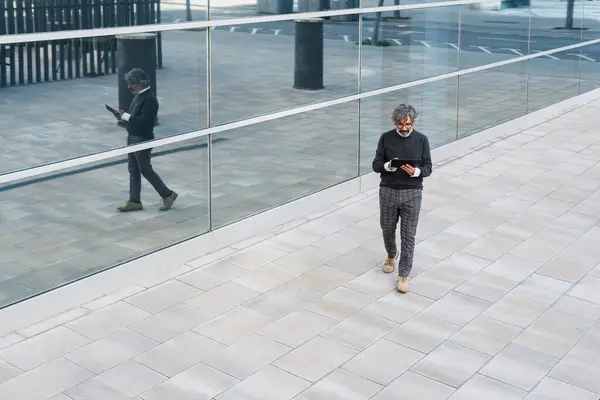 Ofis binasının önünde dijital tablet kullanan olgun, yakışıklı bir iş adamı.
