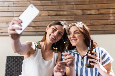 Mutlu genç kadınlar bira şişelerini kızartırken selfie çekiyorlar.