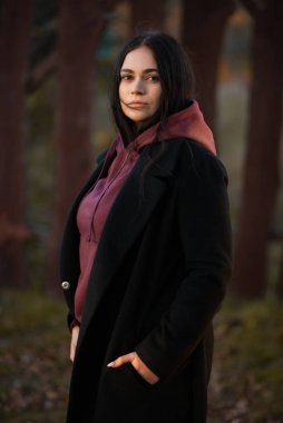 The girl in a black coat and sweater looking confidently at the camera. Autumn portrait