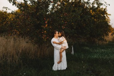 Anne ve kızı gün batımında elma bahçesinde birbirlerine bakıyorlar.