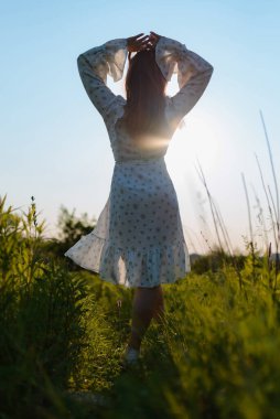 Gün batımında tarlada beyaz elbiseli bir kadının arka görüntüsü.