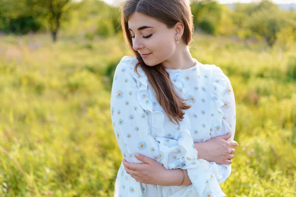 A woman in an elegant dress hugging herself in the field