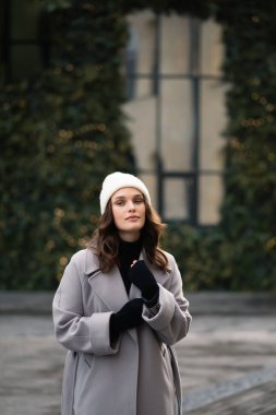 Gri paltolu güzel bir kadın ve sokakta beyaz şapkalı. Kış kıyafeti. Noel konsepti