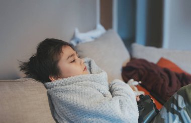 Oturma odasında video oyunu oynayan bir çocuk, online oyun oynayan bir çocuğun portresi kanepede oturup eğlenen bir çocuk, evde tek başına joystick oynayan bir çocuk.