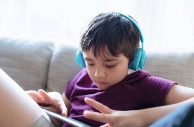 Education concept,High key portrait primary school Kid reading E-book on tablet for homework,Child wearing headphone playing game online on internet,boy sitting on sofa watching cartoon on digital pad