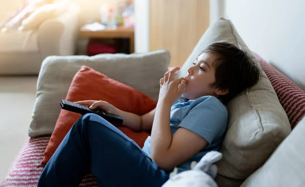 Portrait Kid holding remote control and biting finger nails while watching cartoon on TV, Emotional Young boy deep in thought,Child sitting on couch relaxing in living room,Children Health Care