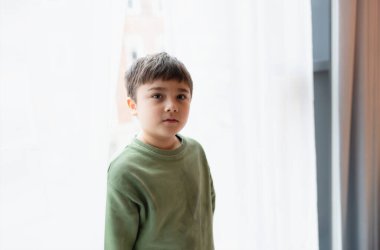 Yüzü gülen çocuk portresi sabah parlak ışıkla dantel perdenin arkasına bakıyor, pozitif çocuk konsepti.