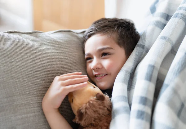 秋の早朝にテレビを見てリラックスしたソファの上に横たわる幸せな少年 快適な子供毛布でソファに横になり 笑顔で外を見る 肯定的な子供の概念 — ストック写真