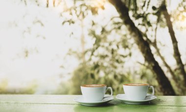Ahşap masa üzerinde kalp şeklinde, bulanık arka planda bir kahve. Sonbahar, kış ya da sonbahar için iki fincan sıcak kahve, kahvaltı için içecekler, kahve molası.