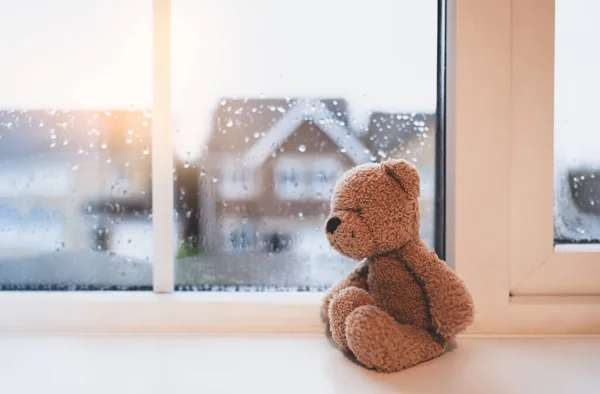 Lonely bear toy sitting alone looking out of window, Sad teddy bear doll sitting next to window in rainy day, Loneliness, Abuse concept, International missing Children day