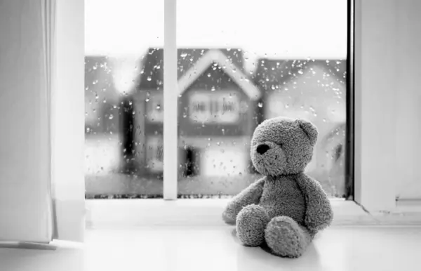Lonely bear toy sitting alone looking out of window,Black and White Sad teddy bear doll sitting next to window in rainy day, Loneliness, Abuse concept, International missing Children day
