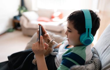 Okula dönüyorum. Akıllı telefonla ödev yapan bir çocuk düşünüyorum. Evde eğitim konsepti, kulaklıkla portre öğrenci İngilizce öğreniyor. Bağımlı Çocuk oyunu ya da müzik dinlemek