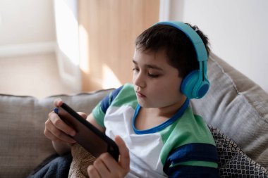 Kulaklık takan, müzik dinleyen, akıllı telefonuyla ödev yapan, kulaklıkla portre okuyan, İngilizce öğrenen bir çocuk.