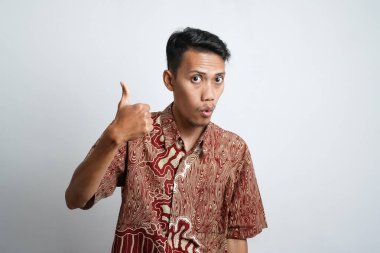 young asian man with brown skin wearing a batik shirt happy expression with joy and showing a thumbs up if he agrees, good, topnotch, white background.