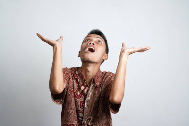 Şok olmuş, batik tişörtlü bir Asyalı beyaz arka planla izole edilmiş, üzerindeki fotokopi alanını işaret ediyor.