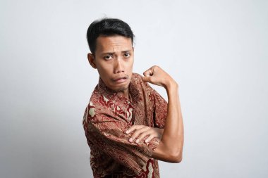 The Asian man looks haggard wearing a batik shirt showing muscular and non-muscled arms