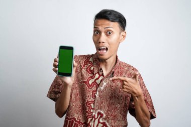 Batik gömlek giyen gülümseyen Asyalı bir adamın portresi ve telefonunda beyaz arka planla izole edilmiş yeşil ekran var.
