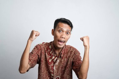 Batik tişört giyen heyecanlı Asyalı adam gururla gülümseyerek kollarını ve kaslarını kaldırarak güçlü bir hareket sergiliyor.