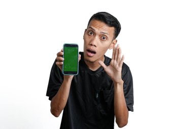 excited asian man wearing black workout t-shirt, pointing at green screen of smartphone. Isolated by white background