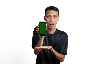 excited asian man wearing black workout t-shirt, pointing at green screen of smartphone. Isolated by white background