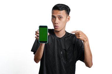 excited asian man wearing black workout t-shirt, pointing at green screen of smartphone. Isolated by white background