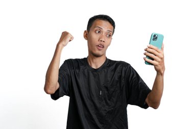 Asian man wearing black training t-shirt, With a happy excited gesture while looking at the smartphone screen. Isolated by white background
