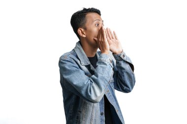 asian man wearing blue jean jacket shouting giving information with hand near mouth, isolated on white background