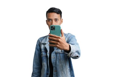 Asian man wearing stylish blue jean jacket holding smartphone looking at camera. Isolated by white background