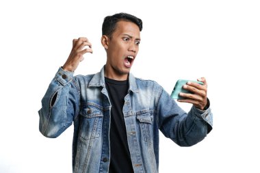 Asian man wearing blue jean jacket surprised expression looking at smartphone screen. Isolated by white background