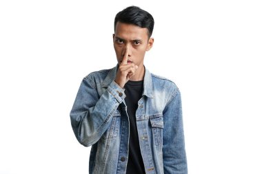 Asian man wearing blue jean jacket gesturing silence, don't make noise. Isolated by white background