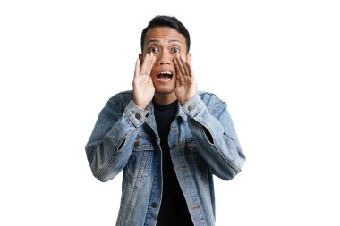 asian man wearing blue jean jacket shouting giving information with hand near mouth, isolated on white background
