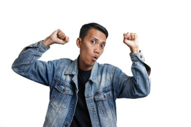 Asian man wearing blue jean jacket doing victory gesture, hands clasped. Isolated by white background