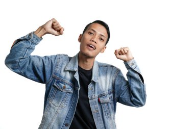 Asian man wearing blue jean jacket doing victory gesture, hands clasped. Isolated by white background