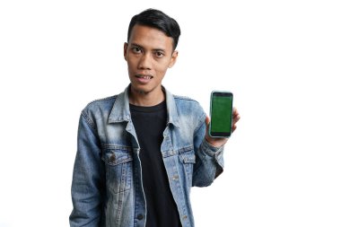Asian man wearing blue jean jacket happy expression pointing at smartphone green screen. Isolated by white background