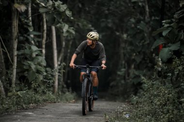 Cyclist in helmet rides bicycle on country road. Using a gravel bike for an uphill route. : Yogyakarta, Indonesia - 28 January 2023