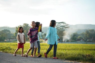 Bantul, Endonezya - 16 Nisan 2023: pirinç tarlalarının kıyısındaki kırsal yollarda arkadaşlarla sabah yürüyüşü.