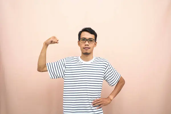 Asian man with glasses wearing casual striped shirt, fist fist pose, indicating strong or ready to fight. Isolated beige background.