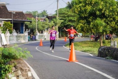 Jogja Maratonu 42K 'nın katılımcıları veya koşucuları, Prambanan tapınak köyünün etrafından güzel bir yoldan geçiyorlar. : Yogyakarta, Endonezya - 18 Haziran 2023